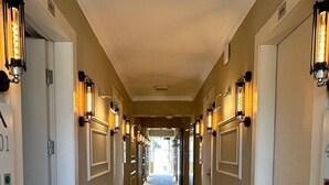 Un pasillo de hotel con pisos alfombrados, puertas numeradas 01 y 04, y luminarias fijadas a la pared.
