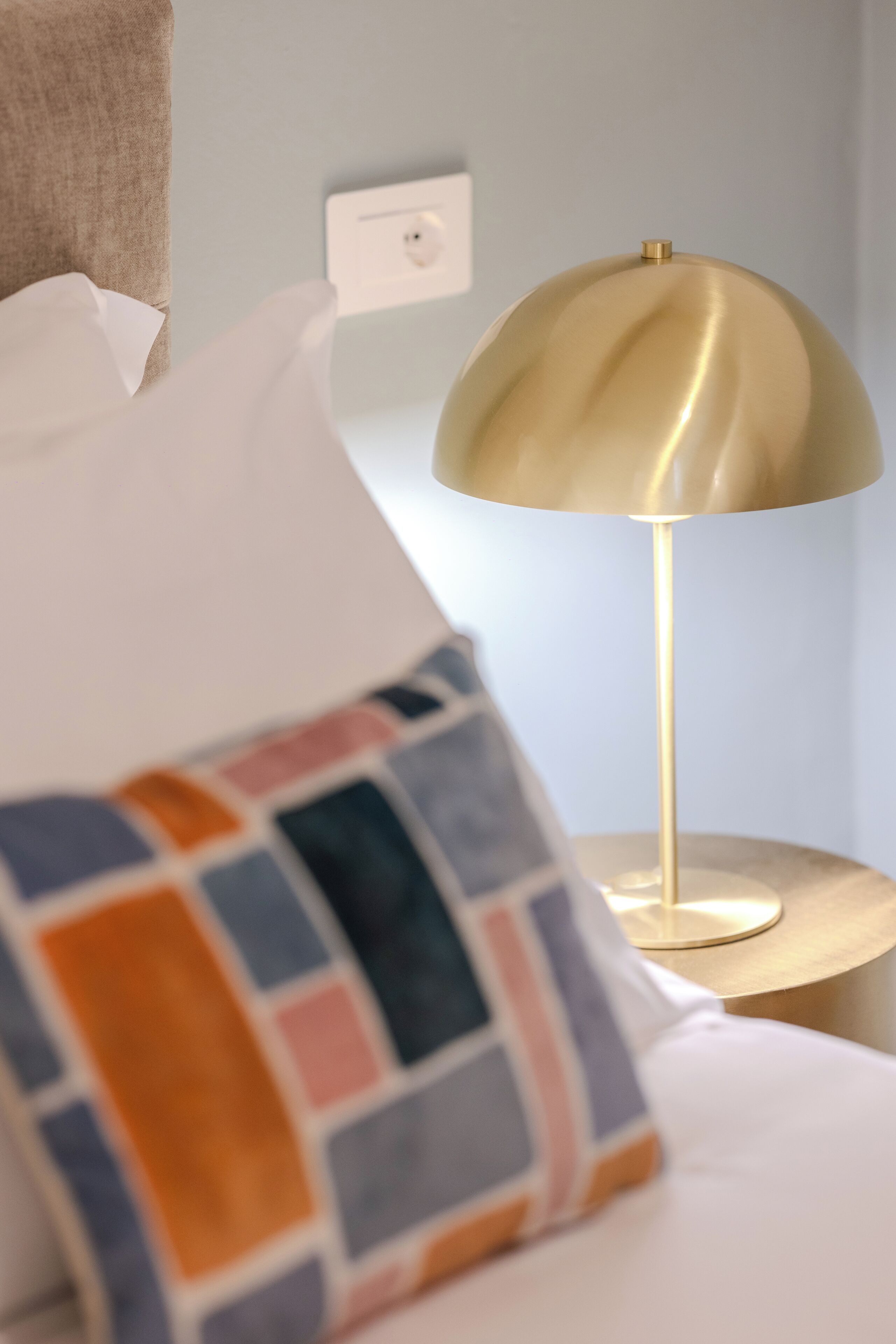 A bed with a patterned pillow and a gold-colored lamp on a bedside table.