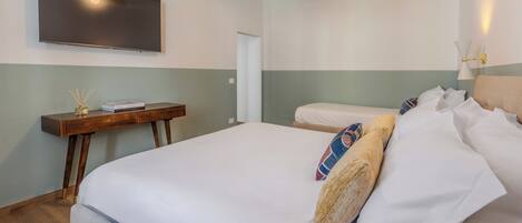 A hotel room with a large bed, a bedside table with a book and a vase, a flat-screen TV mounted on the wall, and a wall-mounted lamp.