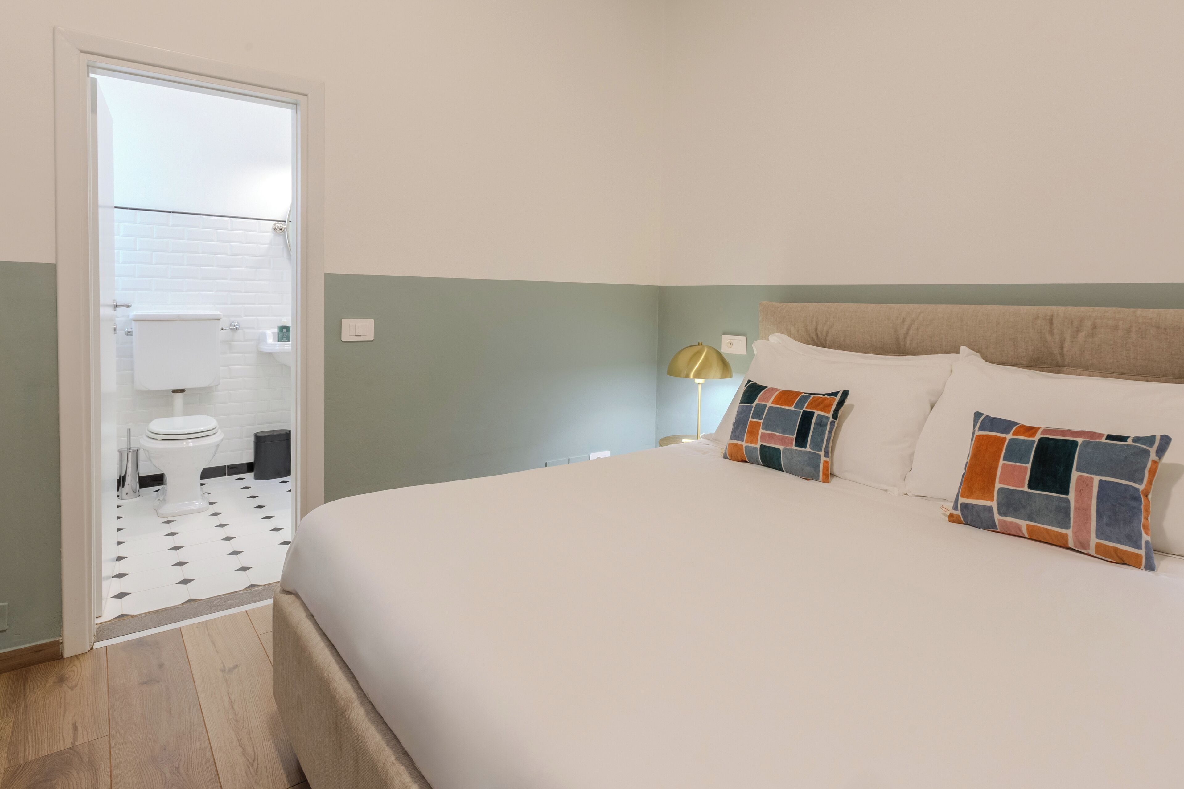 A bedroom with a bed, a nightstand, a lamp, and a view of the bathroom.