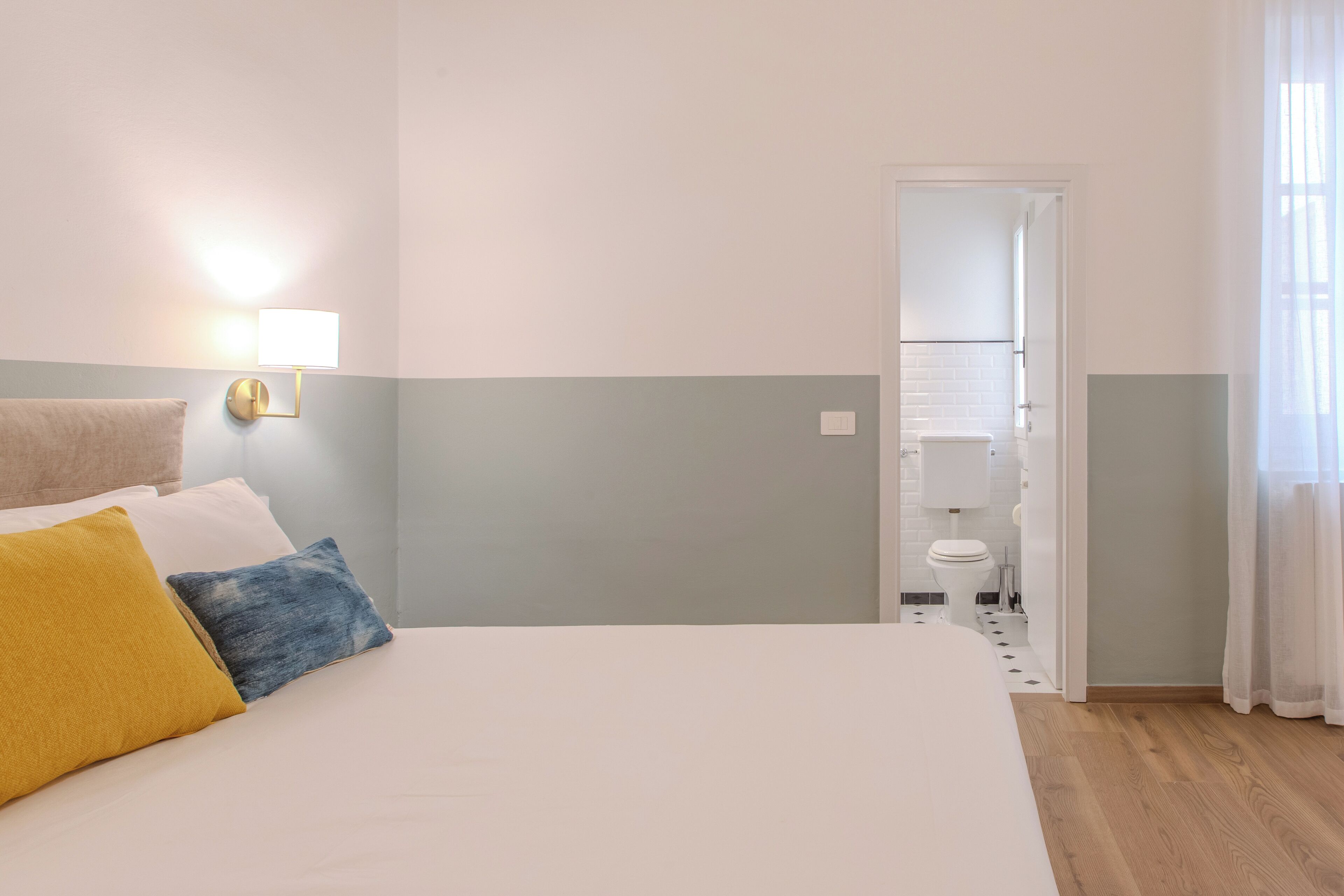 A hotel room with a bed, a wall-mounted lamp, a towel, and a view of the bathroom.