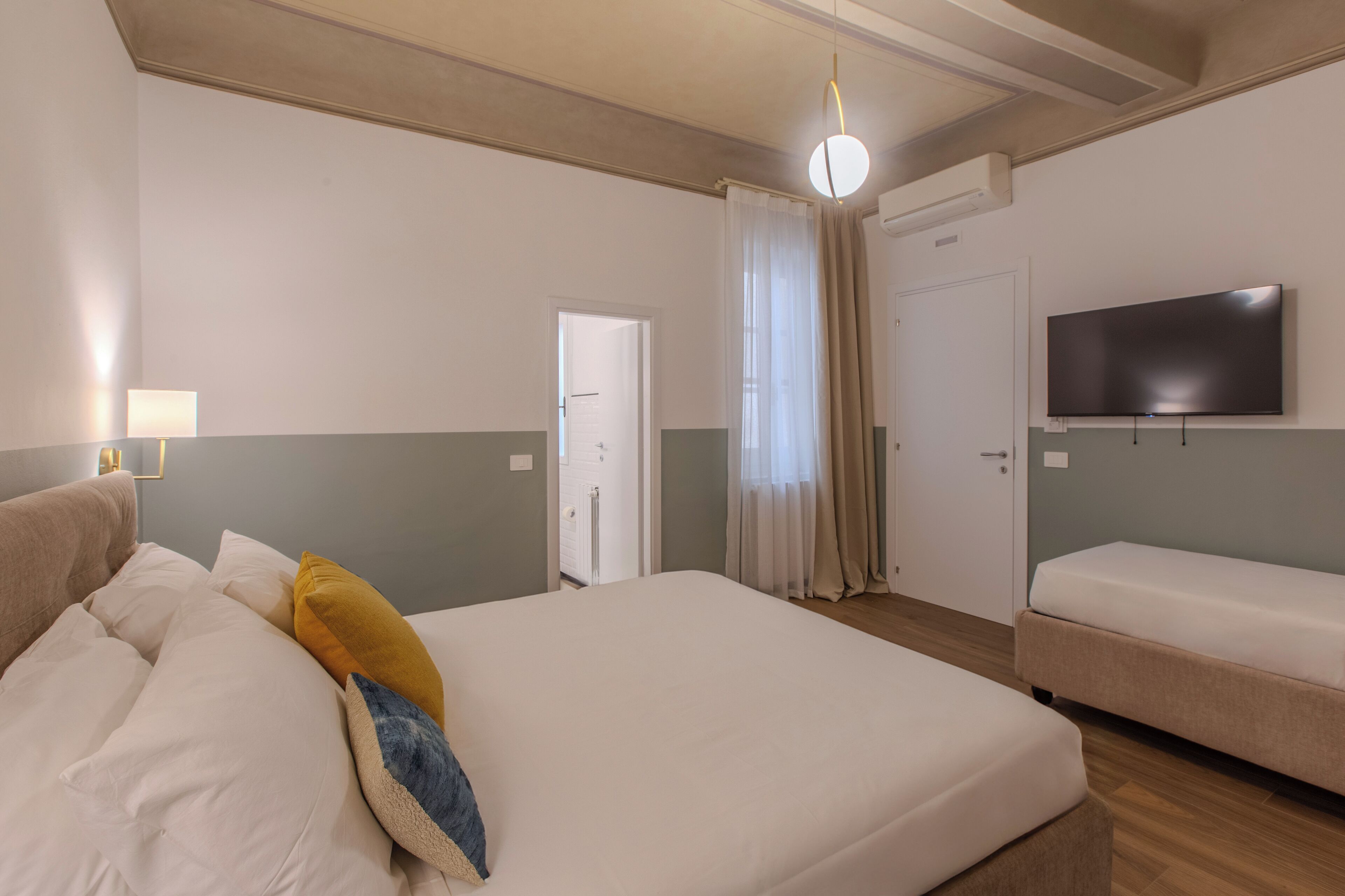 A hotel room with a large bed, a TV, a bedside table, and a door leading to a bathroom.