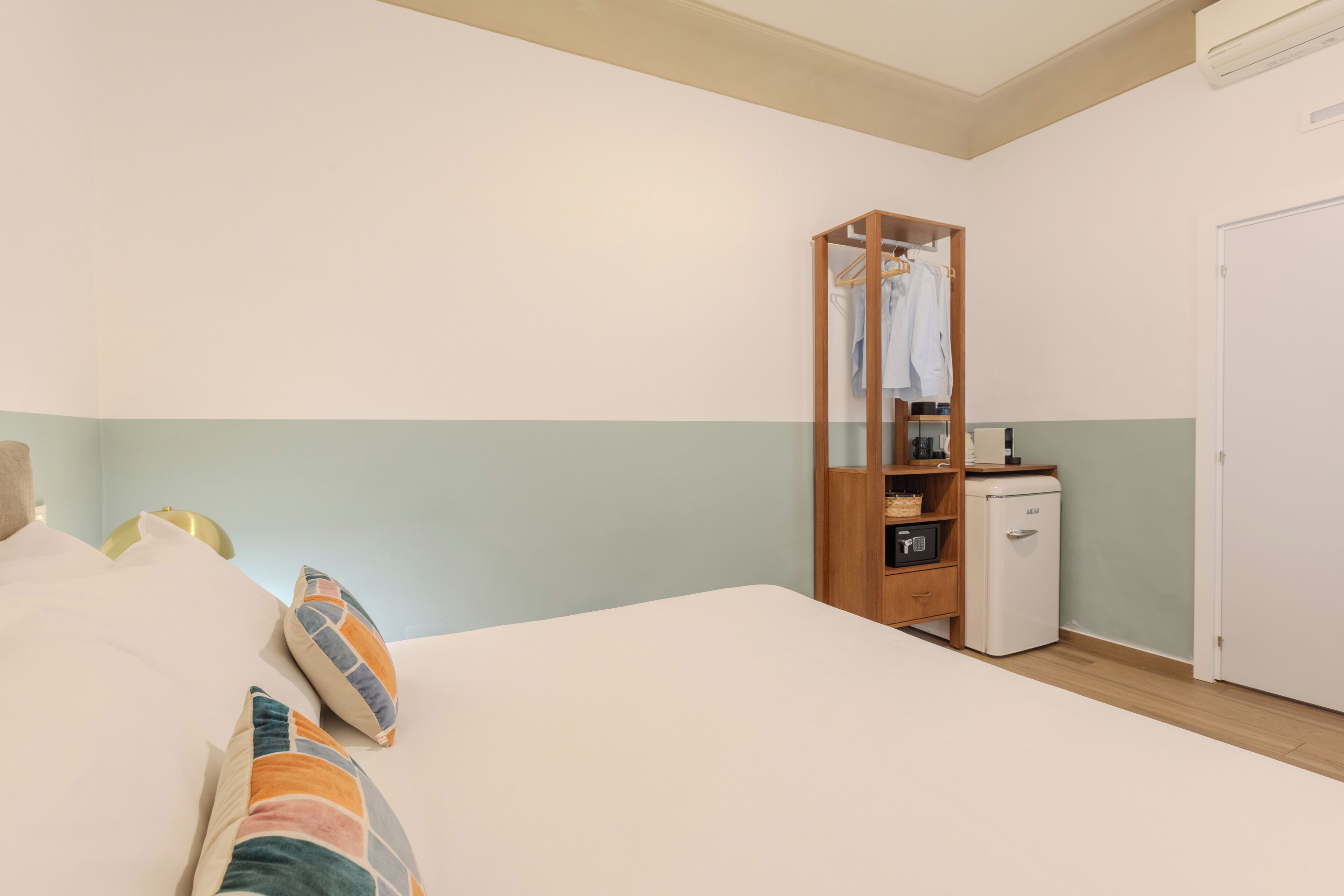 Een slaapkamer met een bed, kussens, een kledingkast, een kleine koelkast en een deur.