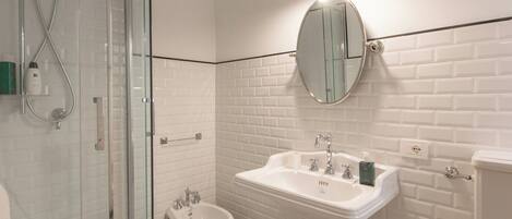 A bathroom with a glass shower enclosure, a white pedestal sink, and a bidet.