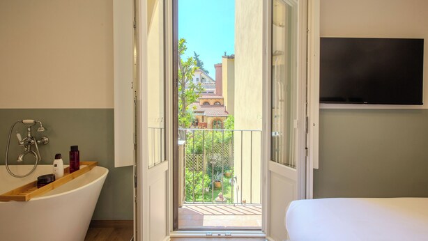 A bathroom with a bathtub, a shower, and a toilet. There is a balcony with a view of buildings and greenery. - B&B Stanze Guelfe (Florence)