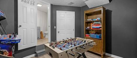 Una habitación con mesa de fútbol, estantería y una puerta.
