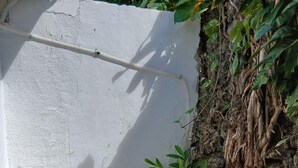 A small outdoor patio with white metal chairs and a table, surrounded by a white wall and a plant-covered wall. - Managua Inn (Managua)