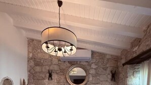 Una camera da letto con parete in pietra, un letto con lenzuola bianche, un comodino, uno specchio e una lampada a sospensione.