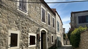 Una stretta strada acciottolata, fiancheggiata da edifici in pietra con portali ad arco e persiane in legno.