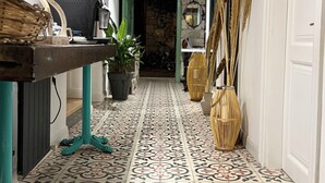 Un corridoio con piastrelle a motivi decorativi, una scrivania con un computer, una pianta in vaso e una lampada a sospensione.
