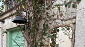 Un edificio rustico in pietra con una porta verde, uno specchio in vimini e una sedia in metallo bianco.