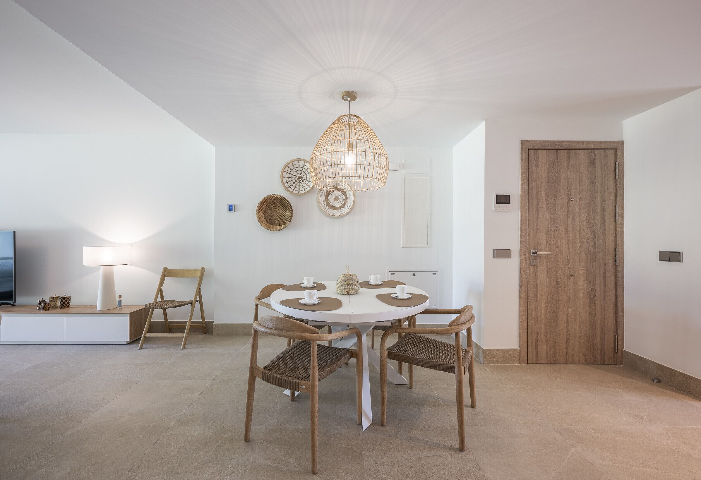 Un coin repas comprenant une table ronde, quatre chaises, un luminaire suspendu et une porte en bois.