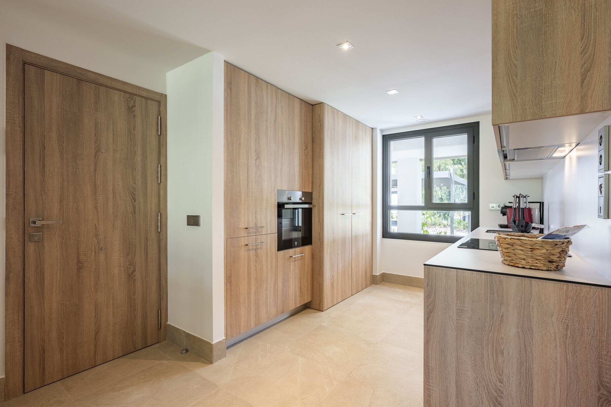 Een moderne keuken met houten keukenkastjes, een inbouwoven en een groot raam dat voor daglicht zorgt.