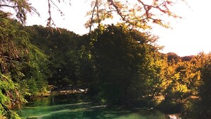 Deux personnes sautent dans une piscine naturelle aux eaux cristallines, entourée de rochers et d’arbres.