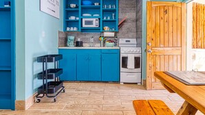 Une cuisine avec des armoires de couleur turquoise, un four à micro-ondes, une cuisinière et une machine à café. On y trouve une porte en bois portant le numéro 4, un panneau sur le mur et un chariot à étagères.
