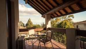 A covered outdoor patio with a table and chairs, a small round table with a bowl, and a view of trees and buildings in the background. - Bonaventura House - House near Mount Etna (Unknown)