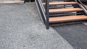 Un escalier métallique menant à l’entrée d’un bâtiment, avec un sol recouvert de gravier.