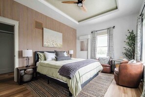 A modern bedroom with a bed, bedside tables, a ceiling fan, a window with curtains, and a plant. - Luxury Historic Suite on Main Street! (Fredericksburg)