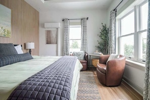 Un dormitorio con una cama, una silla, una mesita y una ventana.