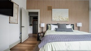 Une chambre à coucher comprenant un lit, des lampes de chevet, un téléviseur et une porte donnant sur une salle de bain.