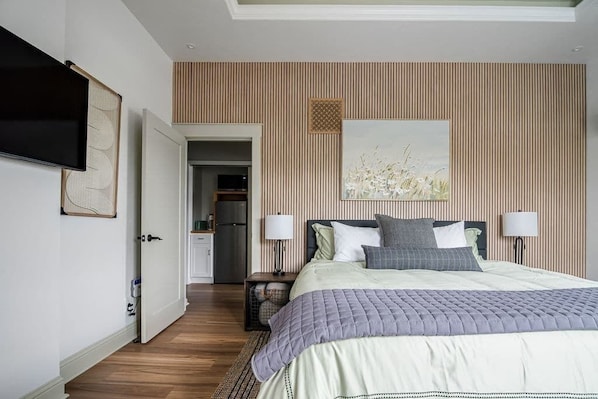 A bedroom with a bed, bedside lamps, a television, and a door leading to a bathroom.