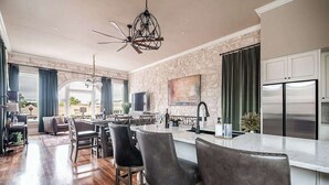 Une cuisine spacieuse dotée d’un îlot central, de chaises en cuir foncé, d’un lustre et d’un mur d’accent en pierre.