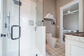 Een badkamer met een douchecabine van glas, een toilet en een wastafel met een marmeren blad.