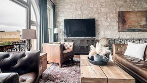 Un salon moderne avec un mur en pierre, un téléviseur à écran plat, des canapés en cuir et une grande fenêtre avec des rideaux.