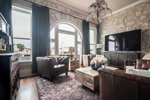A living room with a stone wall, a large TV, leather sofas, and a patterned rug.