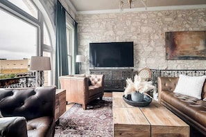 Un salon moderne avec un mur en pierre, un téléviseur à écran plat, des canapés en cuir et une grande fenêtre avec des rideaux.
