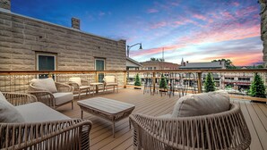 A wooden deck with wicker furniture and a view of the cityscape at sunset. - The Bank on Main St - Downtown Escape Featuring a Deck w/Main St Views! (Fredericksburg)