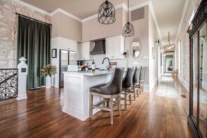 A spacious kitchen with a central island, white cabinetry, and a long hallway leading to a dining area.