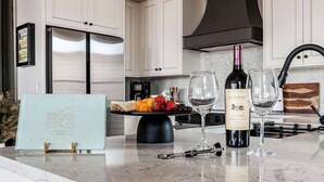 A kitchen with white cabinets, a stainless steel refrigerator, a wine bottle, and glasses on the counter. - The Bank on Main St - Downtown Escape Featuring a Deck w/Main St Views! (Fredericksburg)