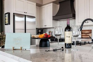 A kitchen with white cabinets, a stainless steel refrigerator, a wine bottle, and glasses on the counter.