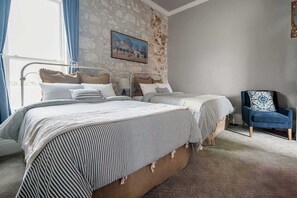 Une chambre avec deux lits, un mur en pierre, un tableau et une chaise bleue.