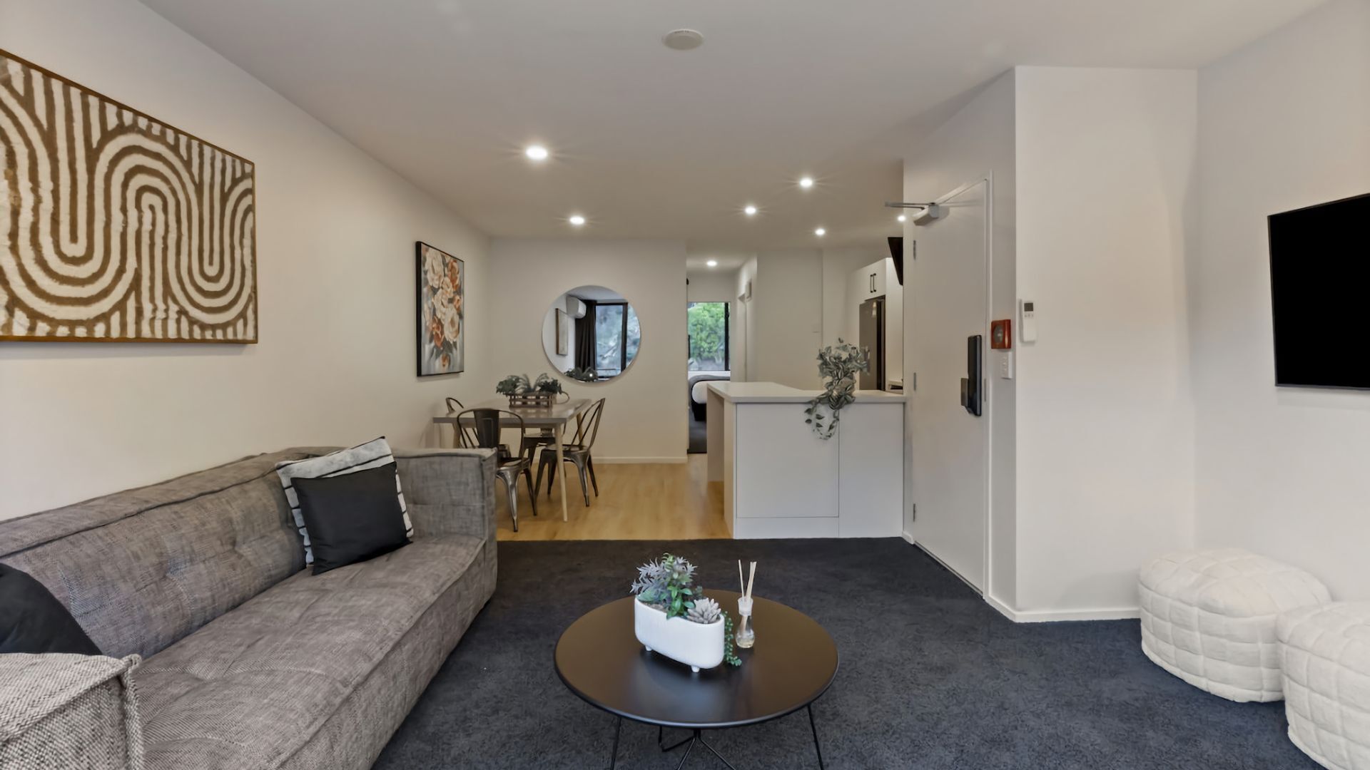 A modern living room with a grey sofa, a round coffee table with a plant, and a dining area with a table and chairs.