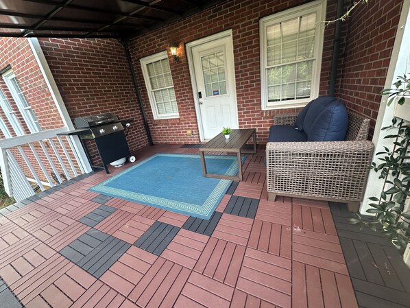 Un patio techado con piso de ladrillo, una piscina pequeña, una silla de mimbre y una mesa.