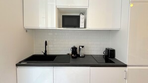 A kitchen with white cabinets, a black countertop, a microwave, a coffee maker, and a sink. - L'appartement Plaisance (Paris)