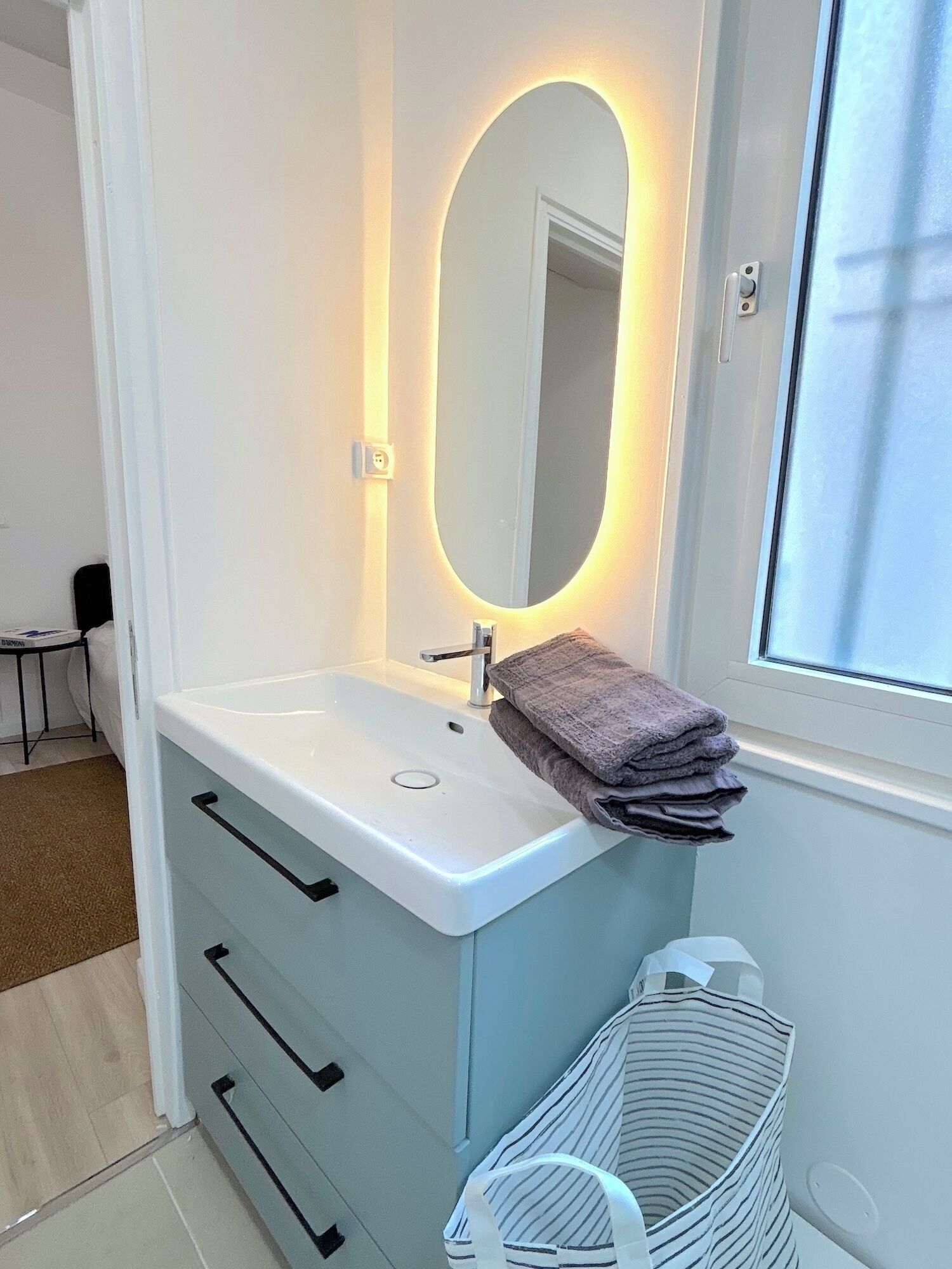 Een badkamer met een wit wastafel, een spiegel met een ovaal lijstwerk, en een raam.