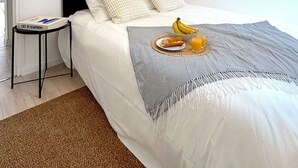 A neatly made bed with white bedding, a grey throw blanket, and a fruit plate. A small table with a book is beside the bed. - L'appartement Plaisance (Paris)