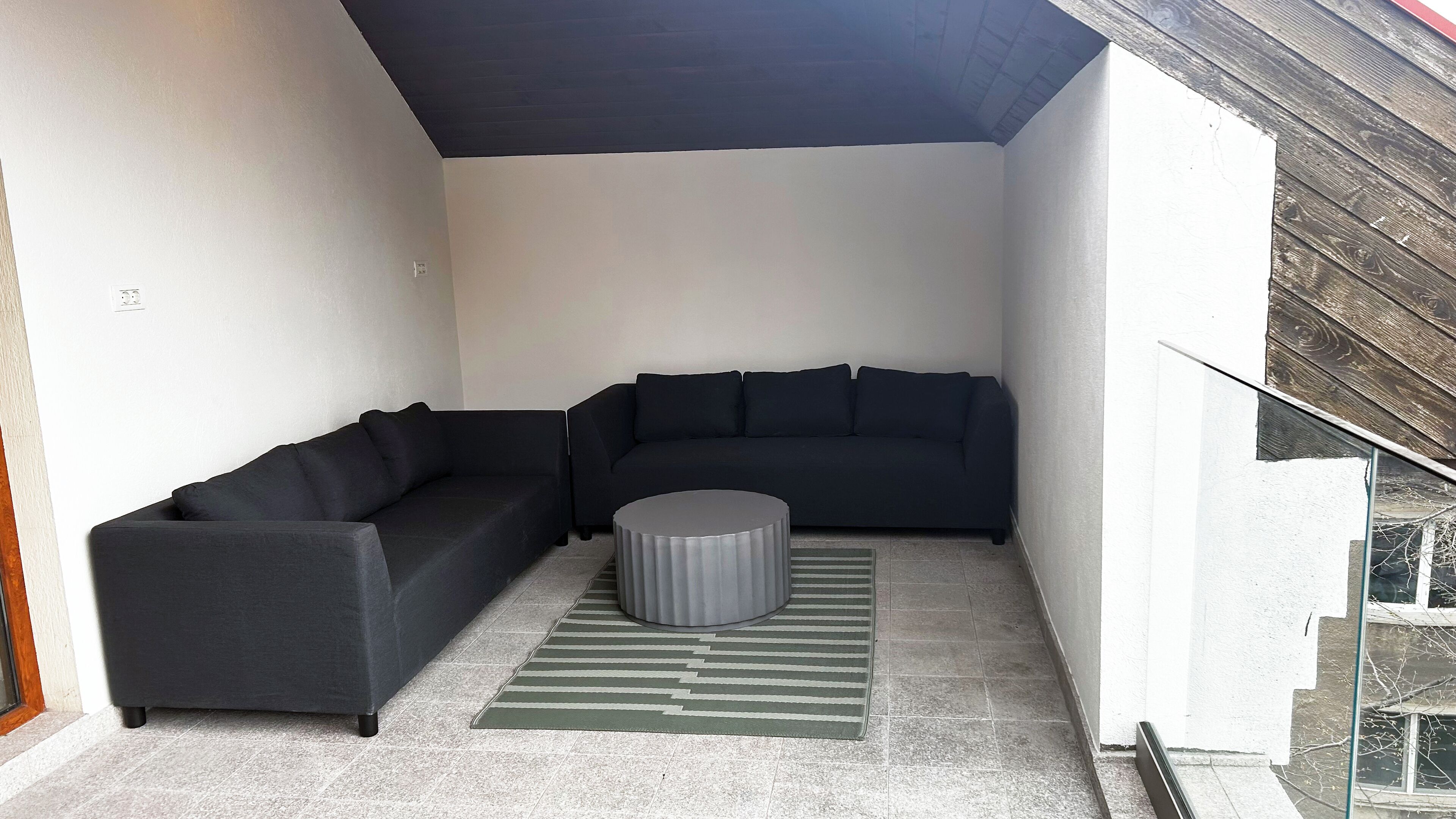 Un salon moderne avec un canapé d’angle gris foncé, un pouf rond gris et un tapis à rayures.
