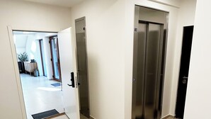 Un hall d’entrée spacieux avec un sol carrelé, un espace d’accueil doté d’un bureau et de chaises, et deux ascenseurs.