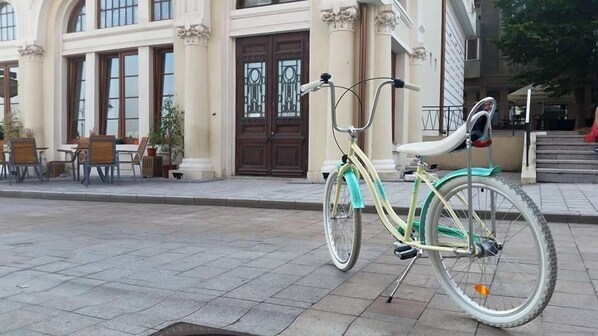 A bicycle parked on a paved sidewalk in front of a building with large windows and a door with decorative glass panels. - Casa Damadian (Constanta)