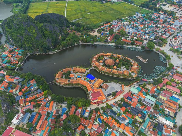 An aerial view of a coastal town with a circular water feature surrounded by colorful buildings and lush greenery. - Heritage Haven (Nam Hoa Lu)