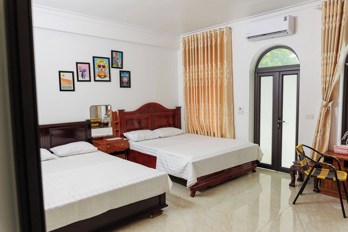 A hotel room with two beds, a wooden headboard, a nightstand, a chair, and a window with curtains.