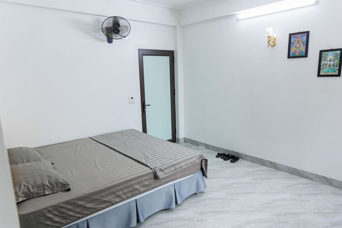 A bedroom with a bed, a door, a fan, and a pair of shoes on the floor.