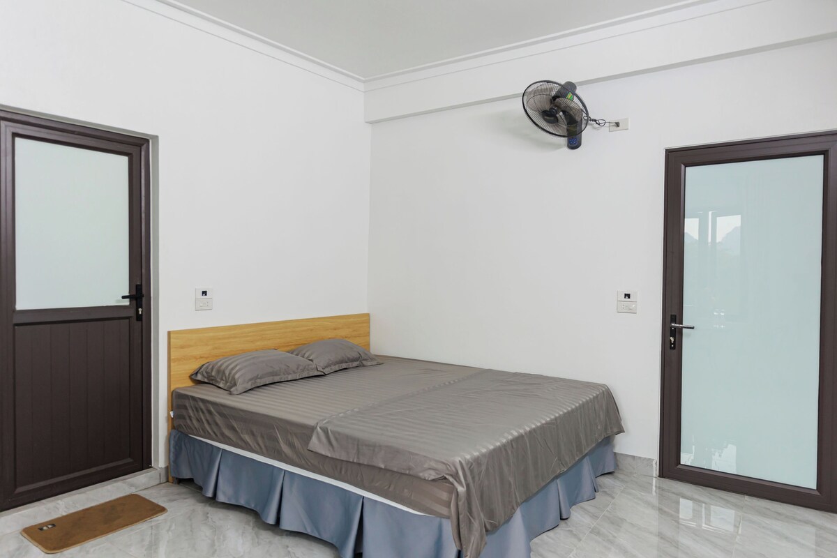 A bedroom with a bed, a wooden headboard, a bedside table, a wall-mounted fan, and a door with frosted glass panels.