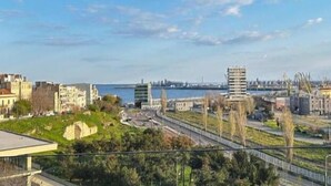 A coastal cityscape with a mix of modern and historical buildings, a clear sky, and a view of the sea. - The Admiral / Luxury Apartment in Constanta (Unknown)