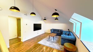 Un salon moderne avec un grand téléviseur, un canapé bleu, une table basse en bois et des lampes suspendues noires.