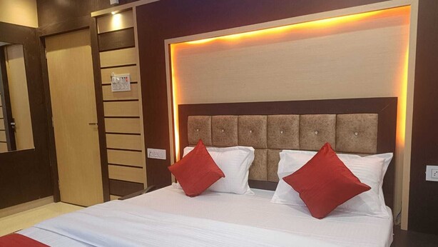 Una habitación de hotel con una cama grande, dos almohadas rojas, un cabecero con iluminación integrada y una pared de paneles de madera.